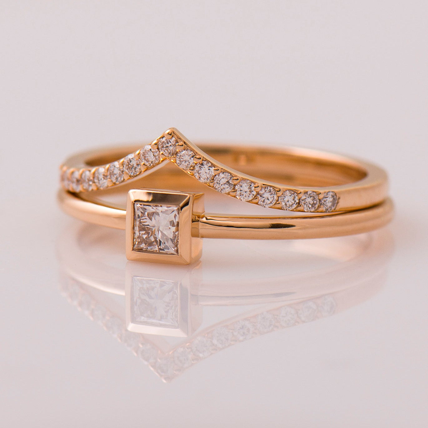 Two gold rings with diamond accents on a reflective surface